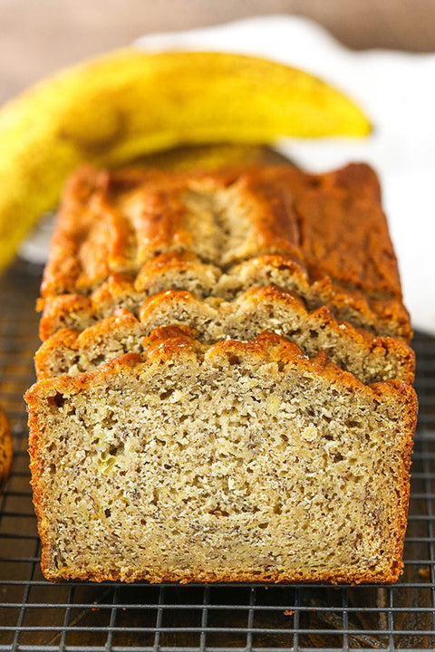 Close-up of banana bread loaf slices with a banana in the background. The image highlights the moist texture and rich, golden-brown crust of the freshly baked banana bread, emphasizing its delicious and inviting appearance. Perfect for showcasing the product's quality and flavor in a visually appealing manner.