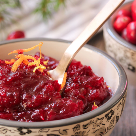 A bowl of homemade cranberry sauce, garnished with orange zest, perfect for Thanksgiving dinner.