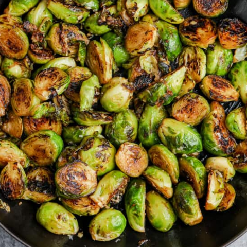 Sautéed Brussels sprouts in a skillet with garlic, butter, and a sprinkle of Parmesan cheese.