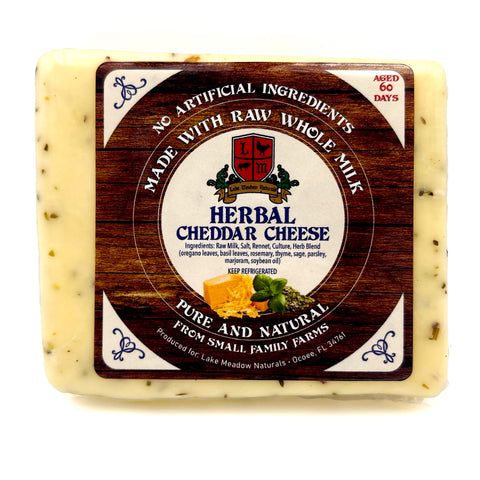 Close-up of Herbal Cheddar Cheese from Lake Meadow Naturals, featuring a label indicating it is made with raw whole milk. The image highlights the cheese's texture and herbal inclusions, emphasizing its rich, natural flavor and high-quality ingredients.