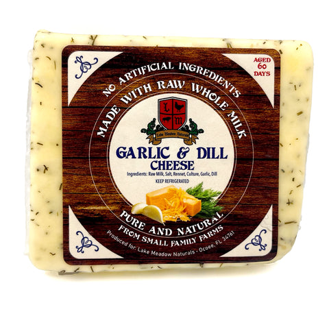 Close-up of Garlic & Dill Raw Milk Cheese from Lake Meadow Naturals, featuring a label with vibrant herbs. The image highlights the cheese’s smooth texture and rich, flavorful combination of garlic and dill. Made with raw whole milk, this artisanal cheese offers a savory, aromatic taste that enhances any cheese board or dish with its gourmet touch.