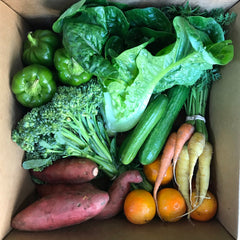 Top view of a CSA produce box filled with fresh organic vegetables, including sweet potatoes, lettuce, broccoli, and leafy greens. This overhead shot highlights the abundance and variety of locally grown, seasonal produce delivered straight to your door